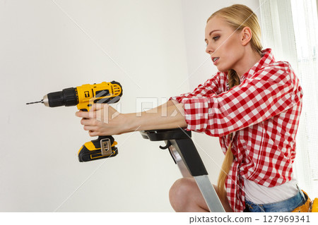 Woman using drill on ladder Woman using drill on ladder 127969341