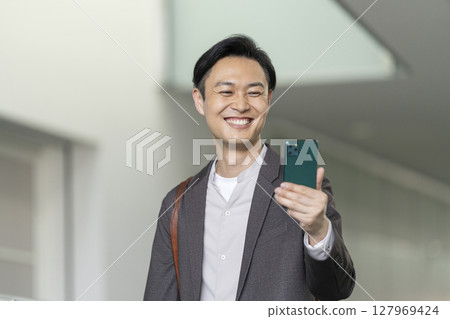 A smiling man in his 40s looking at his smartphone screen 127969424