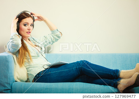 Woman with tablet headphones sitting on couch Woman with tablet headphones sitting on couch 127969477