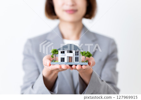 A middle-aged woman in a gray suit holding a model of a house A middle-aged woman in a gray suit holding a model of a house 127969915