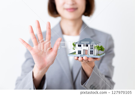 一位身穿灰色西裝的中年婦女手裡拿著房屋模型，伸出五根手指 127970105
