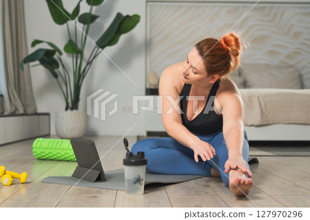 Yoga fitness workout training online. Woman practicing stretching with online app lessons at home. Plus size female doing sports exercise on yoga mat indoor. Girl have training workout for weight loss Yoga fitness workout training online. Woman practicing stretching with online app lessons at home. Plus size female doing sports exercise on yoga mat indoor. Girl have training workout for weight loss 127970296
