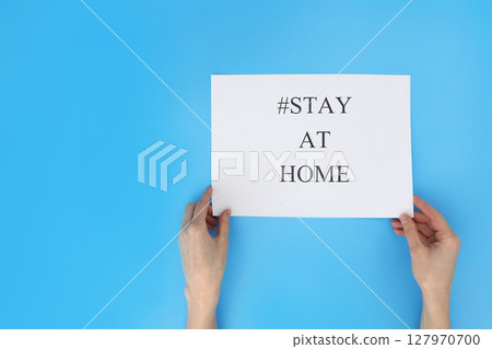 stay at home concept. woman hand holding paper with words stay at home isolated on blue background. Coronavirus, COVID-19, self-quarantine, isolation 127970700