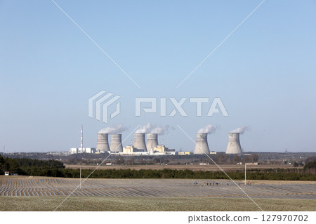 view of a nuclear power plant. View of smoking chimneys of nuclear power plant, power lines and forest, under blue sky with white clouds view of a nuclear power plant. View of smoking chimneys of nuclear power plant, power lines and forest, under blue sky with white clouds 127970702
