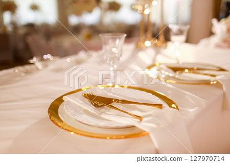 table decoration with pink tablecloth, crystal candlesticks with candles and white pink flowers in restaurant . stylish wedding day. setting table with gold plate, fork and knife table decoration with pink tablecloth, crystal candlesticks with candles and white pink flowers in restaurant . stylish wedding day. setting table with gold plate, fork and knife 127970714