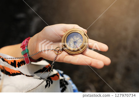 Girl holding compass in the hand. Child exploring nature in the forest on summer sunny day Kid learning how to use compass. Outdoor recreation and awesome adventures with family 127970734