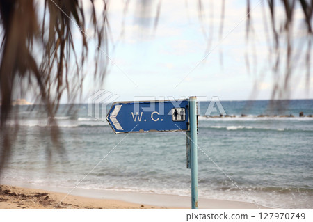 direction to the toilet on the beach. WC - inscription on signboard toilet hanging on a pole, a blue sky background. direction to the toilet on the beach. WC - inscription on signboard toilet hanging on a pole, a blue sky background. 127970749
