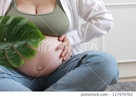 Eco pregnancy. Pregnant woman with big belly advanced pregnancy holding green tropical palm monstera leaf in hand 127970762