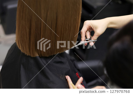 Unrecognisable hairdresser cutting female client hair with professional barber scissors and comb and making stylish haircut short bob hairstyle in beauty salon. Hair care, hair salon and hairstyling Unrecognisable hairdresser cutting female client hair with professional barber scissors and comb and making stylish haircut short bob hairstyle in beauty salon. Hair care, hair salon and hairstyling 127970768
