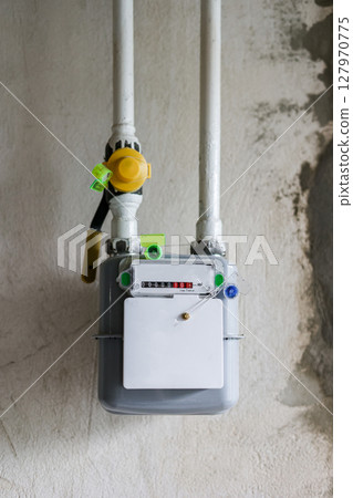 Vertical photo of gas meter and pipes, on concrete wall in a house under renewal. Indoor gas meter used for measuring natural gas consumption in residential buildings, houses. Energy crisis in Europe Vertical photo of gas meter and pipes, on concrete wall in a house under renewal. Indoor gas meter used for measuring natural gas consumption in residential buildings, houses. Energy crisis in Europe 127970775