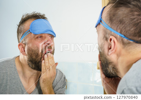 Sleepy man looking at mirror and yawning Sleepy man looking at mirror and yawning 127970840