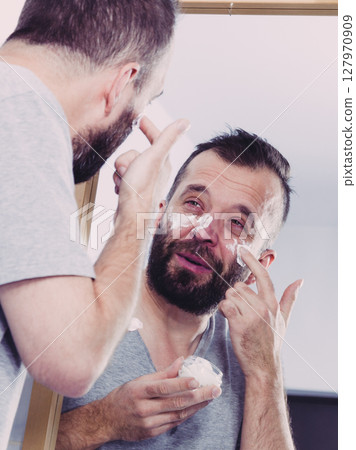 Man applying moisturizer cream in bathroom 127970909