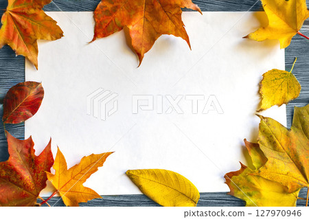 Blank white mockup surrounded by brightly colored autumn leaves on wooden background 127970946