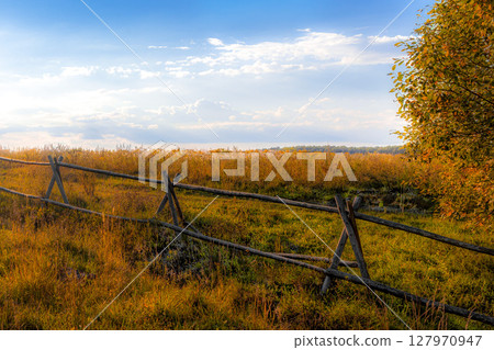 Scenic view of rustic wooden fence in an autumn field with golden grasses under clear blue sky. Captures essence of peaceful countryside charm and seasonal beauty 127970947