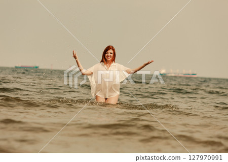 Redhead woman playing in water during summertime 127970991