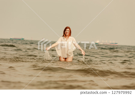 Redhead woman playing in water during summertime 127970992