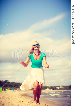 Blonde woman wearing dress playing jumping on beach Blonde woman wearing dress playing jumping on beach 127971161