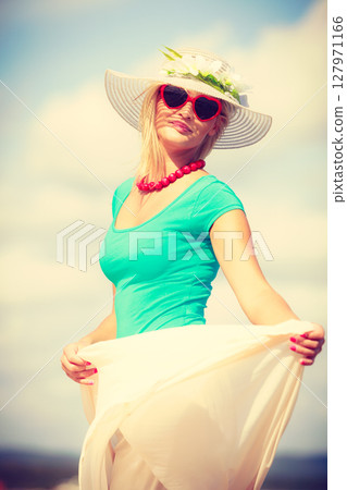Blonde woman wearing dress walking on beach Blonde woman wearing dress walking on beach 127971166