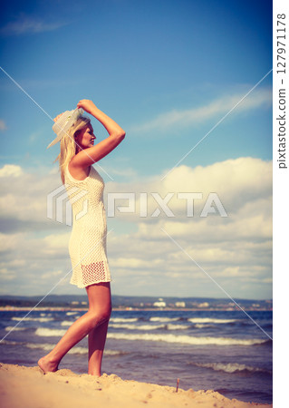 Blonde woman wearing dress walking on beach Blonde woman wearing dress walking on beach 127971178