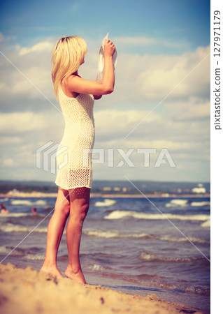 Blonde woman wearing dress walking on beach Blonde woman wearing dress walking on beach 127971179