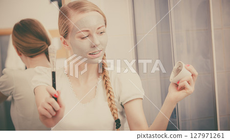 Happy young woman applying mud mask on face Happy young woman applying mud mask on face 127971261