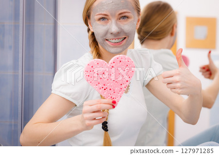 Woman having grey face mask holding heart sponge Woman having grey face mask holding heart sponge 127971285