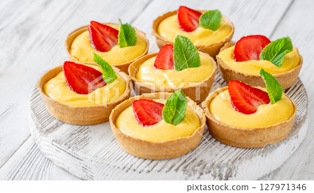 Mini mango cream tarts with strawberry and mint on white wooden board Mini mango cream tarts with strawberry and mint on white wooden board 127971346