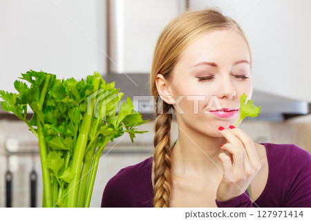 Woman in kitchen holds green celery 127971414