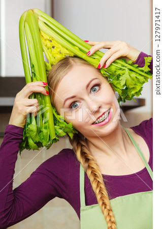 Woman in kitchen holds green celery 127971417