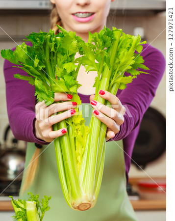 Woman in kitchen holds green celery 127971421