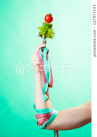 Woman hand with vegetarian food and measuring tapes. Woman hand with vegetarian food and measuring tapes. 127971541
