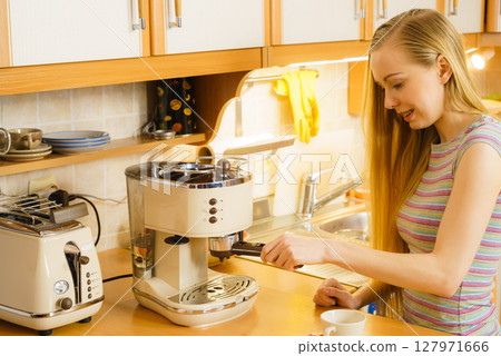 Woman in kitchen making coffee from machine 127971666
