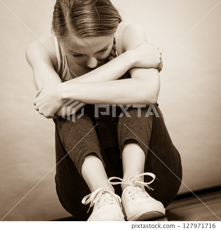 Sad depressed young teenage girl sitting by wall 127971716