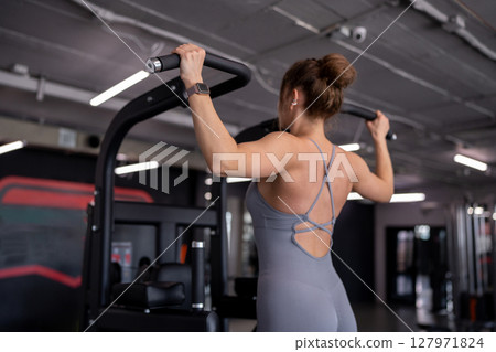 Back, pull up and woman in gym for workout, power and exercise for fitness, body health or strong core. Grip, hanging and athlete on bar for abs or leg raises for balance, training and muscle growth 127971824