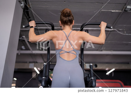 Back, pull up and woman in gym for workout, power and exercise for fitness, body health or strong core. Grip, hanging and athlete on bar for abs or leg raises for balance, training and muscle growth 127971843