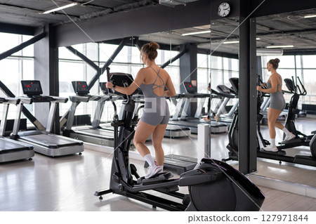 A woman is actively exercising on an elliptical machine at a modern gym facility 127971844