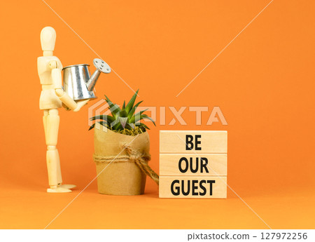 Be our guest symbol. Concept words Be our guest on beautiful wooden block. Businessman model. Beautiful orange background. Business and be our guest concept. Copy space. Be our guest symbol. Concept words Be our guest on beautiful wooden block. Businessman model. Beautiful orange background. Business and be our guest concept. Copy space. 127972256