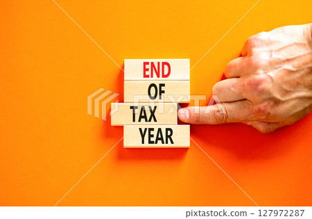 End of tax year symbol. Concept words phrase End of tax year on beautiful wooden blocks. Beautiful orange paper background. Businessman's hand. Business End of tax year concept. Copy space. End of tax year symbol. Concept words phrase End of tax year on beautiful wooden blocks. Beautiful orange paper background. Businessman's hand. Business End of tax year concept. Copy space. 127972287