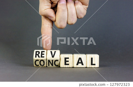 Reveal or conceal symbol. Businessman turns wooden cubes and changes word Conceal to Reveal. Beautiful grey table grey background, copy space. Business reveal or conceal concept. 127972323