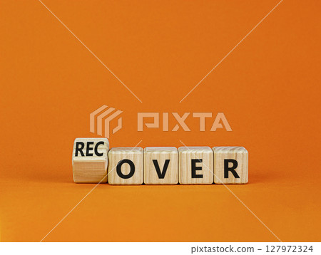 Time to recover symbol. Turned a wooden cube and changed the word 'over' to 'recover'. Beautiful orange table, orange background. Business, over or recover concept. Copy space. 127972324