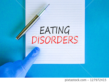 Eating disorders symbol. Concept words Eating disorders on beautiful white note. Doctor's hand in blue medical glove. Beautiful blue background. Medical healthy lifestyle eating disorders concept. Eating disorders symbol. Concept words Eating disorders on beautiful white note. Doctor's hand in blue medical glove. Beautiful blue background. Medical healthy lifestyle eating disorders concept. 127972415