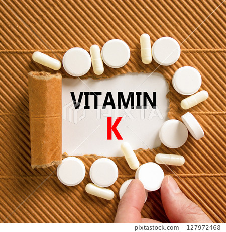Vitamin K phylloquinone symbol. Concept words Vitamin K on beautiful white paper. White pills. Doctor's hand. Beautiful brown background. Medical healthy lifestyle Vitamin K phylloquinone concept. 127972468