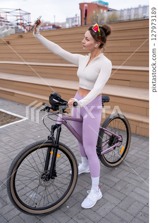 Stylish and Sporty Young Woman is Joyfully Taking a Fun Selfie While Riding Her Bicycle 127973189