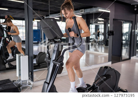 Woman training and fitness in gym on elliptical machine for health, wellness and cardio endurance. Cyclist, exercise bike and performance on equipment, power challenge and intense workout Woman training and fitness in gym on elliptical machine for health, wellness and cardio endurance. Cyclist, exercise bike and performance on equipment, power challenge and intense workout 127973195