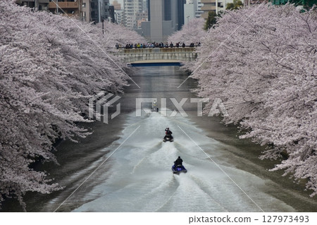 Meguro Ward, Tokyo, Japan - Cherry blossom trees along the Meguro River and the surrounding cityscape - Jet skis on the river, cherry blossoms in full bloom and skyscrapers Meguro Ward, Tokyo, Japan - Cherry blossom trees along the Meguro River and the surrounding cityscape - Jet skis on the river, cherry blossoms in full bloom and skyscrapers 127973493