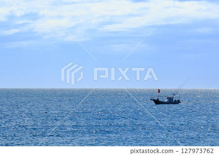 A fishing boat floating on the sea; a patrol boat anchored offshore from the beach 127973762