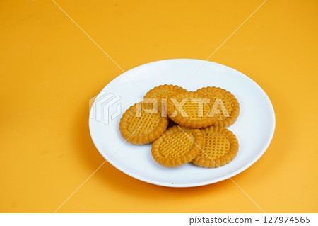 A plate of golden-brown, round, crunchy biscuits with a textured surface, set against an orange background. 127974565