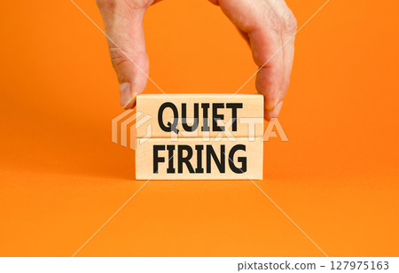 Quiet firing symbol. Concept words Quiet firing on wooden blocks. Beautiful orange table orange background. Businessman hand. Business and quiet firing concept. Copy space. 127975163
