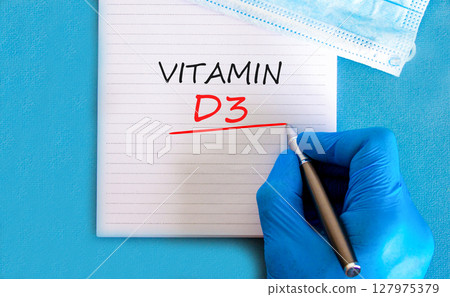Vitamin D3 symbol. Concept words Vitamin D3 on beautiful white note. Doctor's hand in blue medical glove. Medical mask. Beautiful blue background. Medical healthy lifestyle Vitamin D3 concept. 127975379