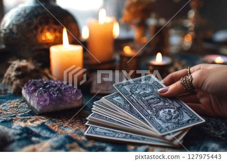 A fortune teller's hand touches a deck of tarot cards on a table, surrounded by candles and amethyst. Tarot layout, concept of astrology and magic spiritual horoscopes A fortune teller's hand touches a deck of tarot cards on a table, surrounded by candles and amethyst. Tarot layout, concept of astrology and magic spiritual horoscopes 127975443